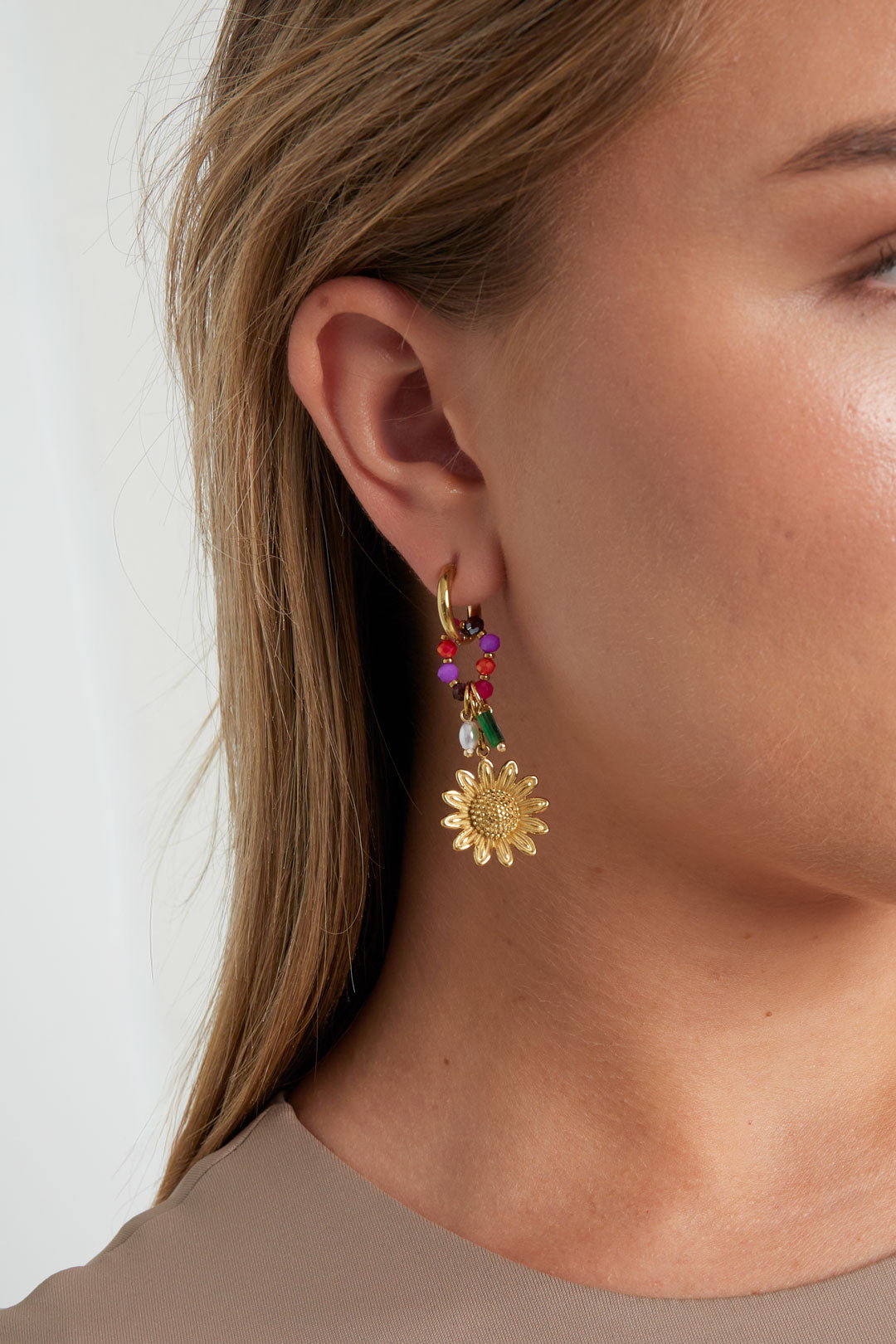 Close-up of a woman wearing gold sunflower charm hoop earrings with colorful beads showing details and fit