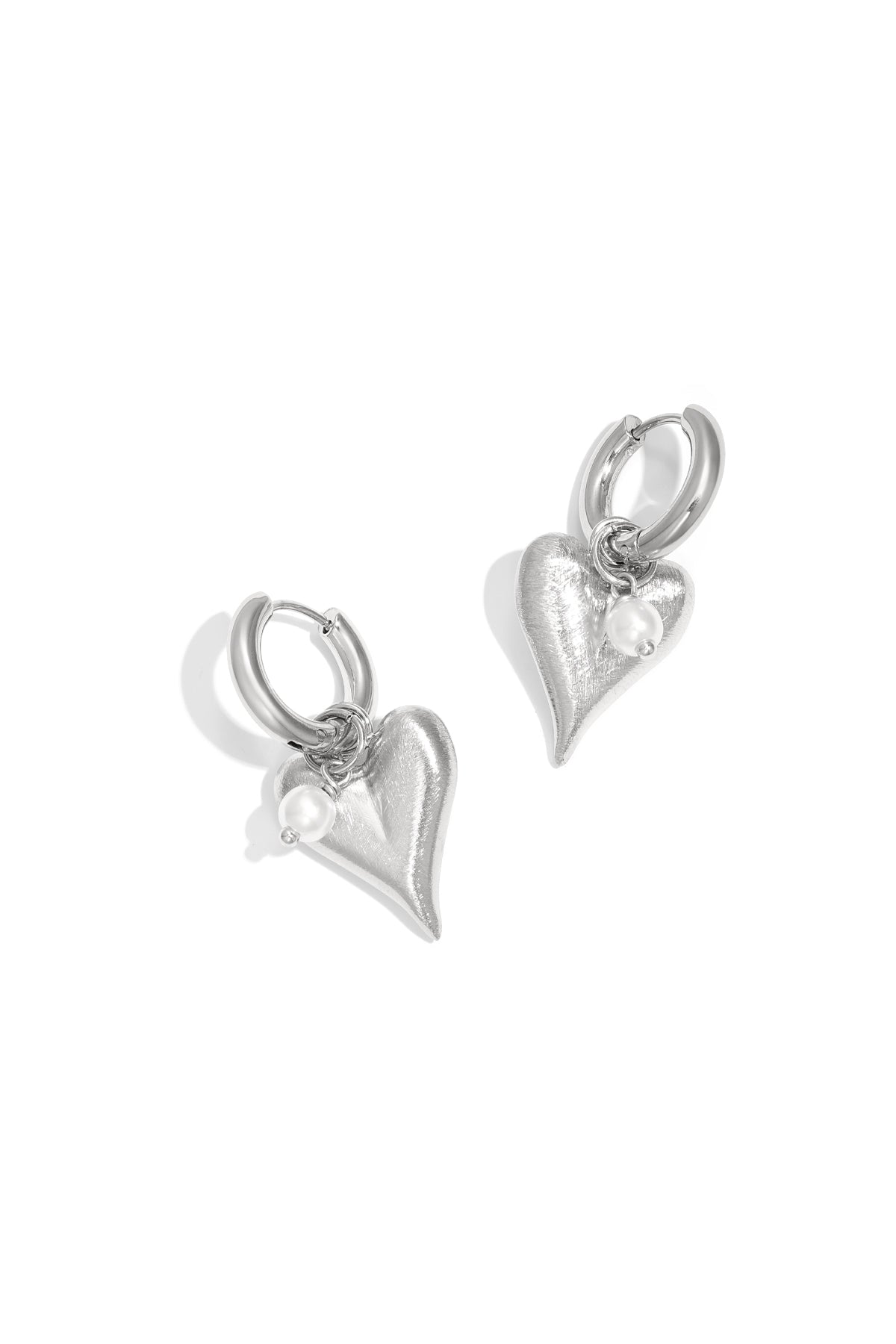 Pair of silver heart charm hoop earrings with pearl detail on white background