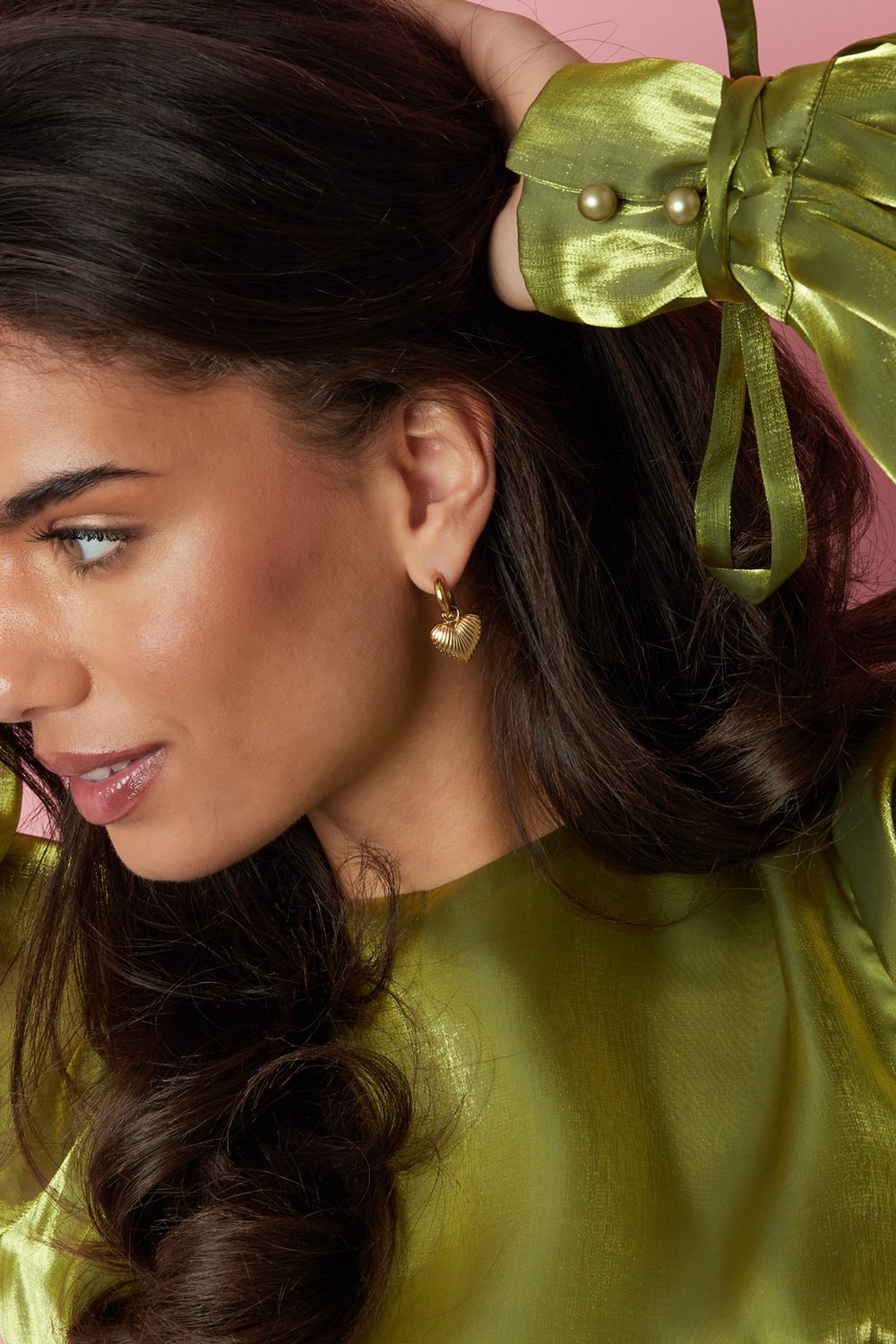 Main Character Heart Drops: gold hoop earrings with a textured, ribbed heart charm worn by a model in a green top.