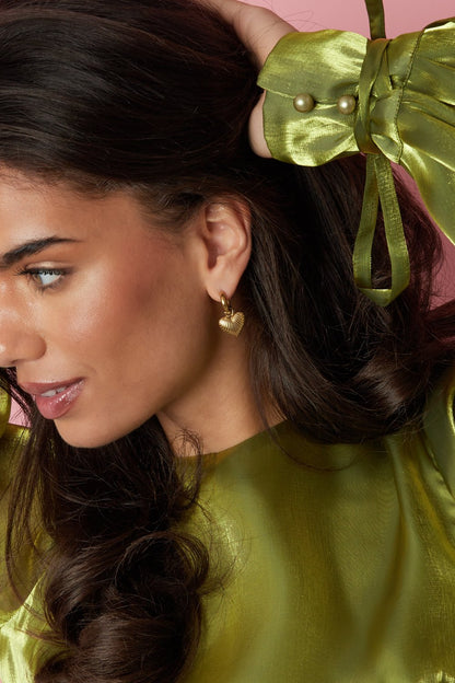 Main Character Heart Drops: gold hoop earrings with a textured, ribbed heart charm worn by a model in a green top.