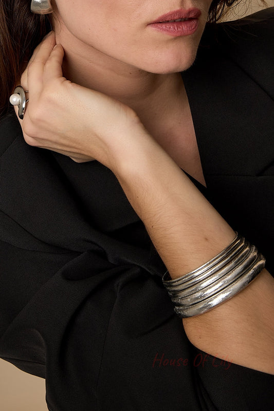 Woman wearing multiple textured silver bangles on wrist paired with black outfit