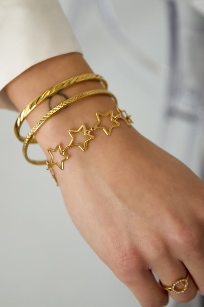 Close-up of a woman's wrist wearing the gold-tone star charm chain bracelet alongside two gold bangles and a ring