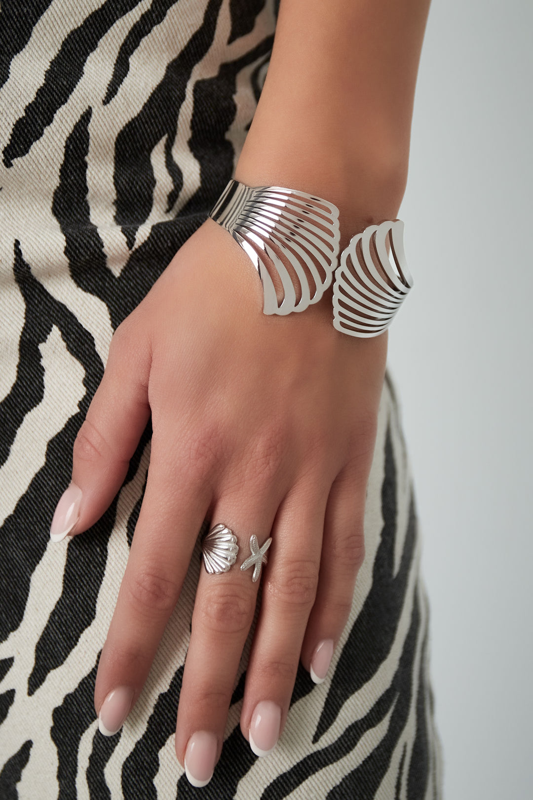 Close-up of a woman wearing silver shell design cuff bracelet and matching shell-and-starfish ring with zebra print dress