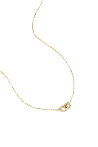 Gold necklace with two intertwined heart charms on a delicate chain, laid flat on white background