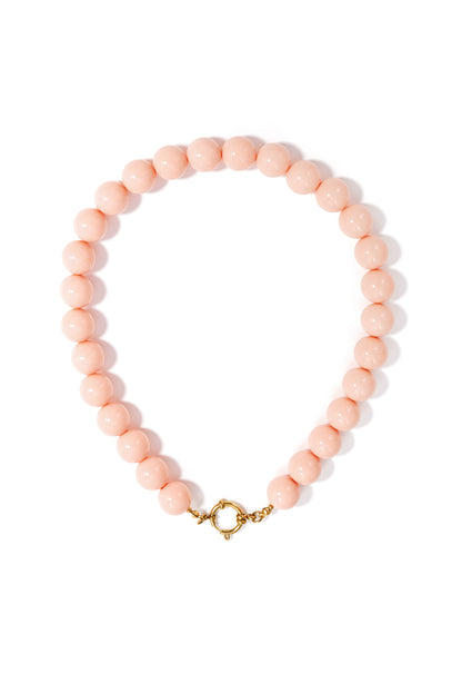 Chunky necklace of smooth, pale pink resin beads with a round gold front-clasp closure on a white background.