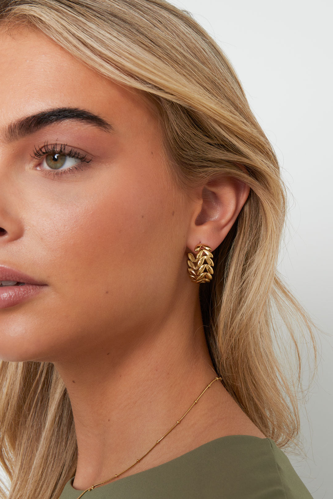 Close-up side view of woman wearing gold leaf motif hoop earring with soft blond hair