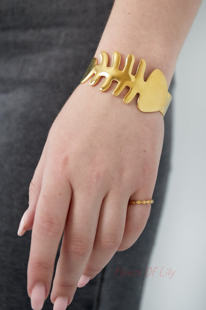 Close-up view of a woman's wrist wearing the shiny gold fishbone bangle and a delicate gold ring with heart pattern