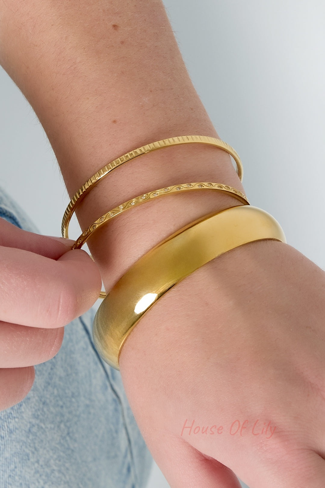 Close-up wrist shot showcasing three gold bangles layered stylishly, highlighting their distinct textures and shine