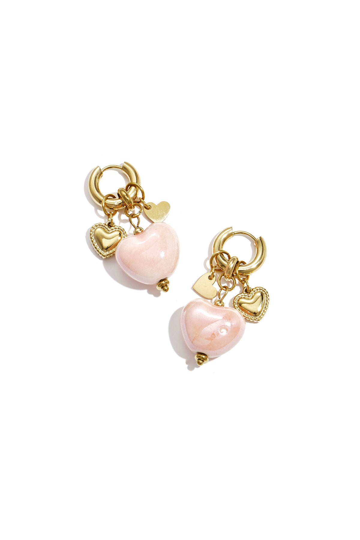 Pair of gold hoop earrings with soft pastel pink glossy heart charms and gold heart pendants on a white background