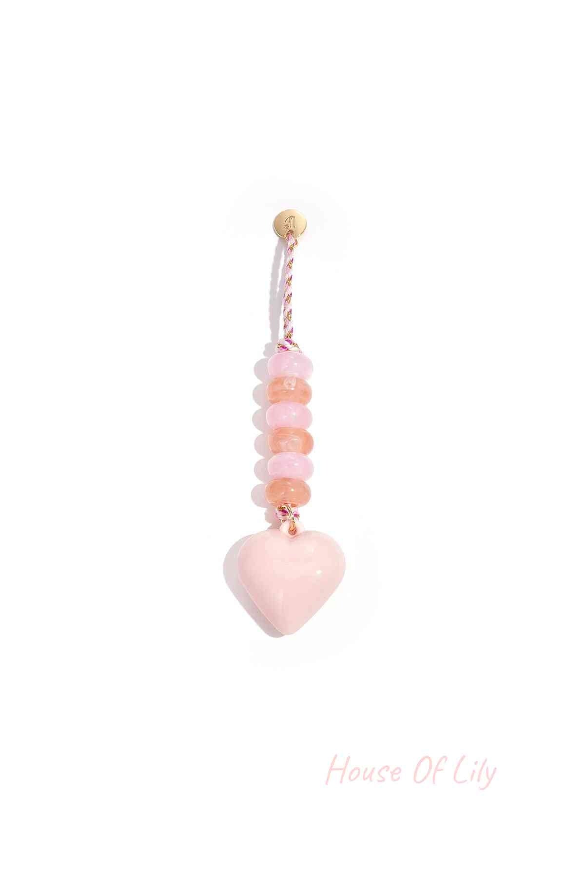 Pastel pink heart-shaped acrylic bag charm with alternating peach and pink beads on braided pink and gold loop hanging alone against white background.