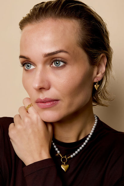 Model wearing gold heart charm hoop earrings with matching ring and pearl necklace close-up