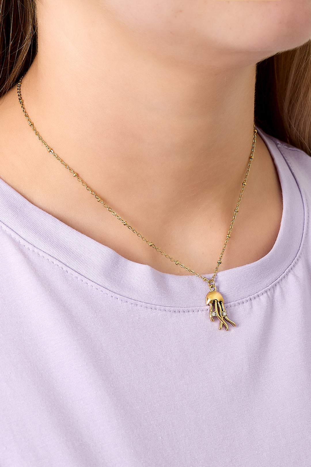 Close-up of gold jellyfish pendant necklace worn on a woman with light purple shirt
