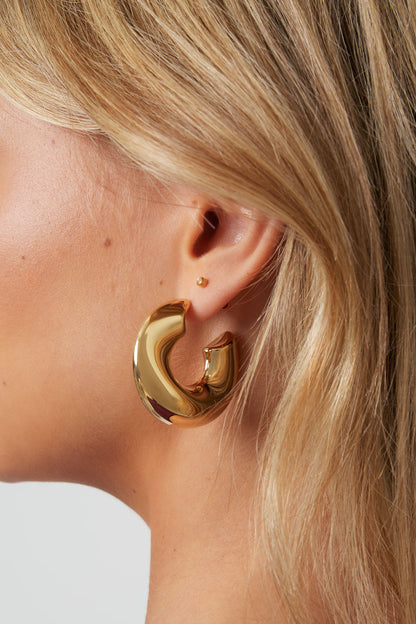 Profile of a woman showcasing the curved shape of the chunky gold sculptural hoop earring
