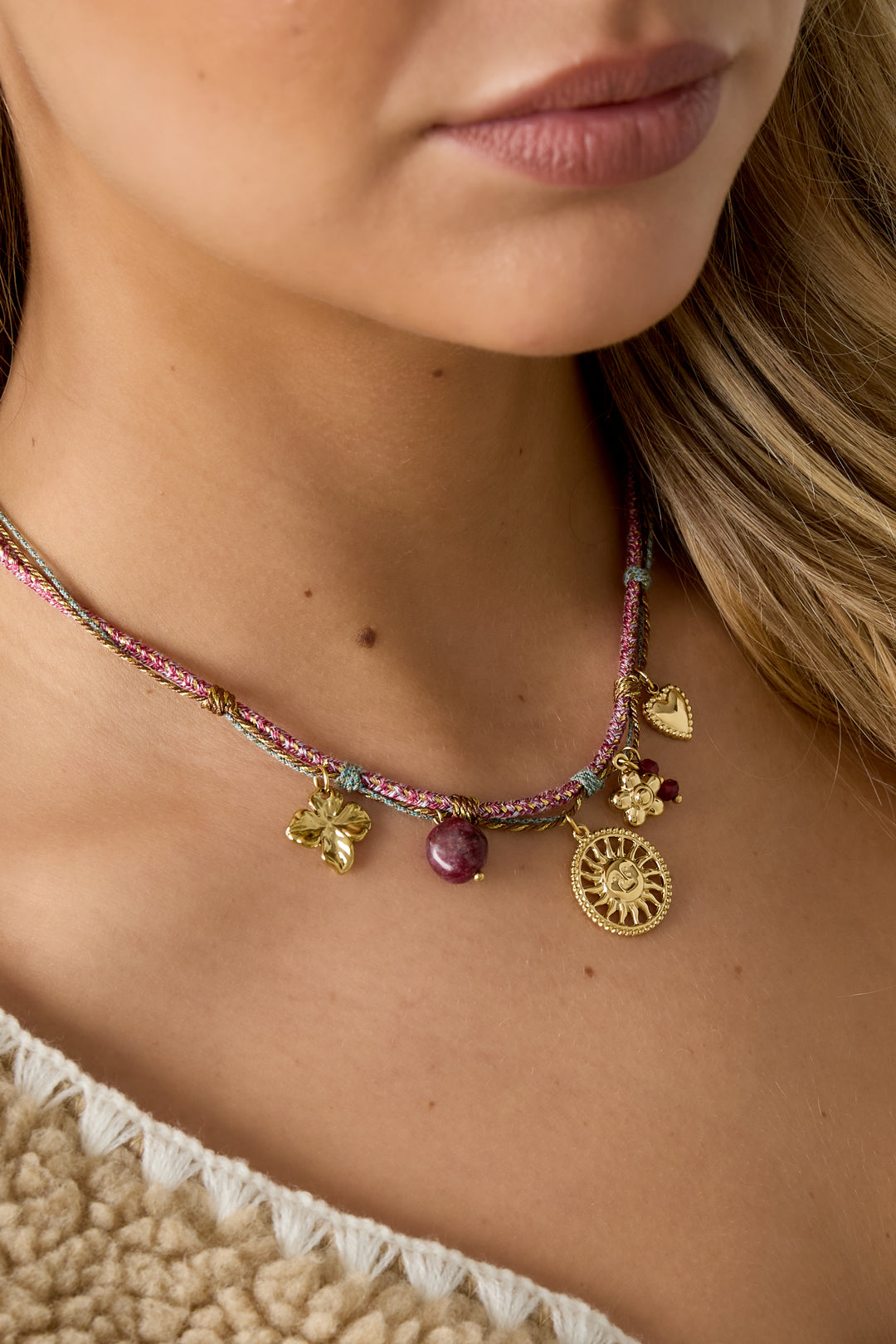 Close-up of necklace worn by woman, showing colorful charm pendant details against skin and cream sweater