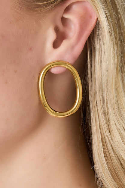 Model wearing one gold oval hoop earring with blonde hair visible