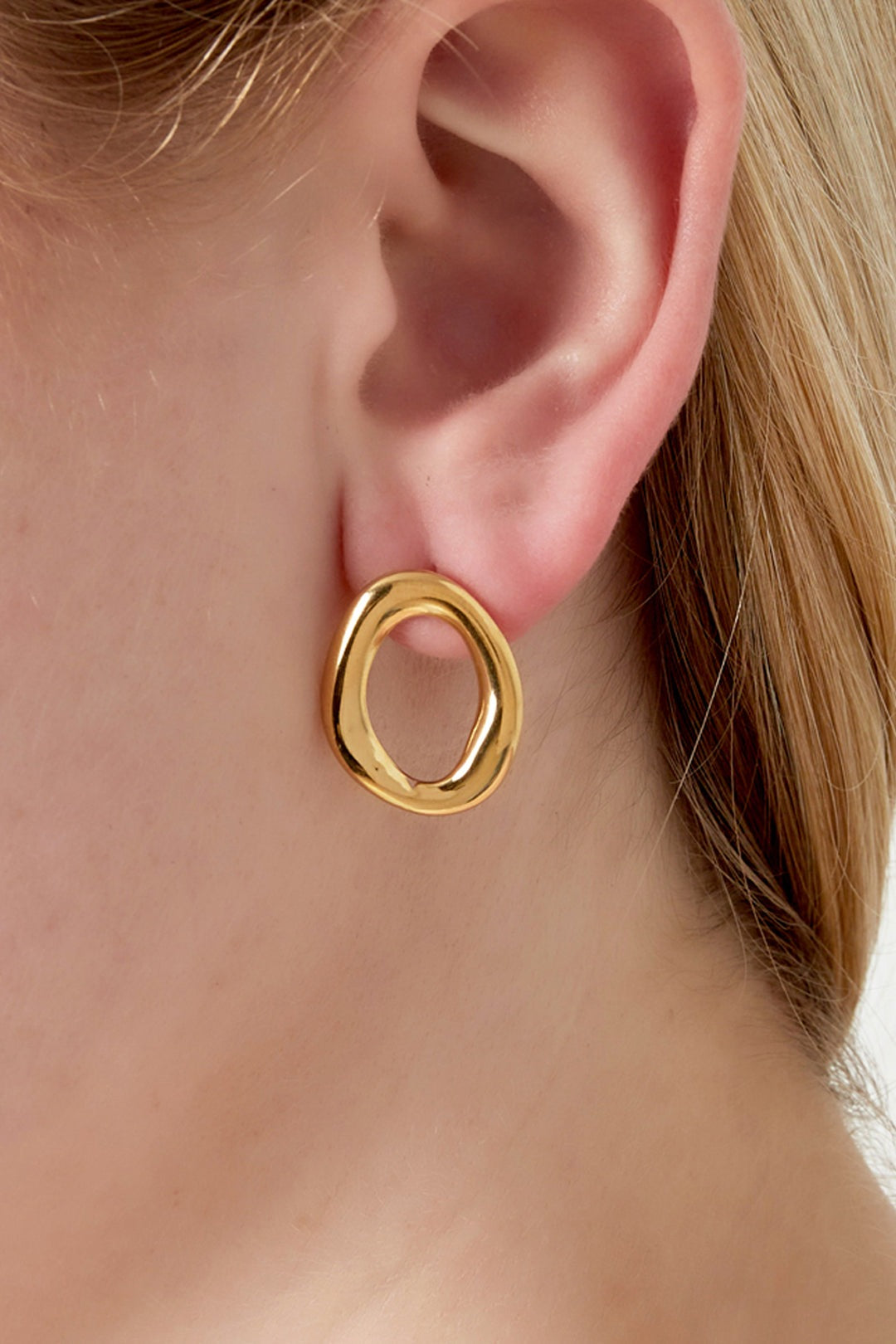 Close-up of gold oval stud earring worn on female ear showcasing soft, shiny finish