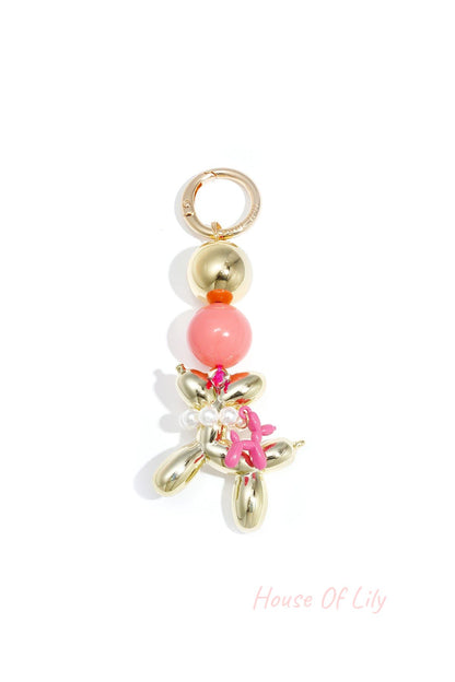 Gold-tone balloon dog keychain with coral pink acrylic bead and small pink balloon charm against white background