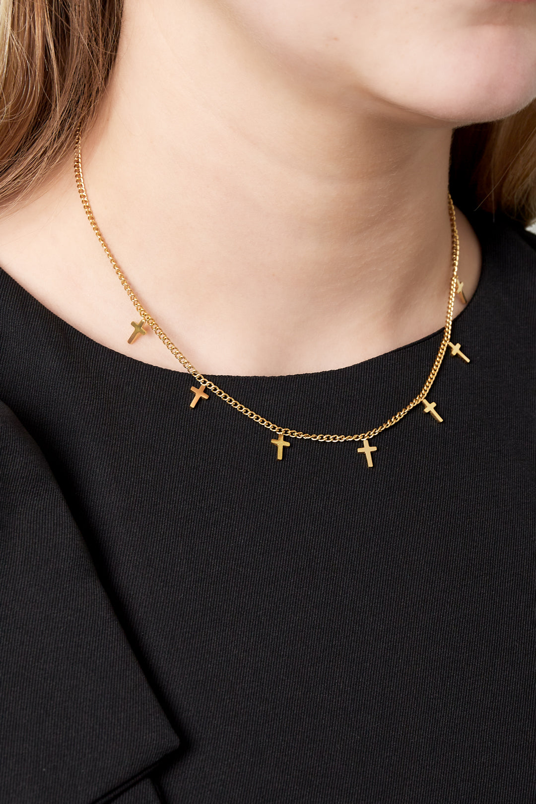 Close-up of necklace worn on a woman, showing gold cross charms on a delicate chain over black top