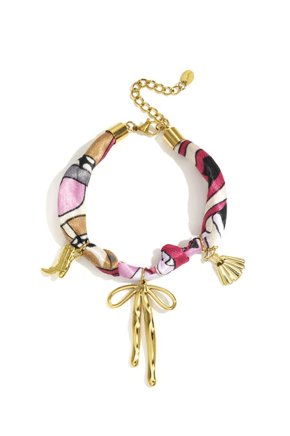 Colorful fabric bracelet with gold-tone bow and charm details laid flat with adjustable gold chain