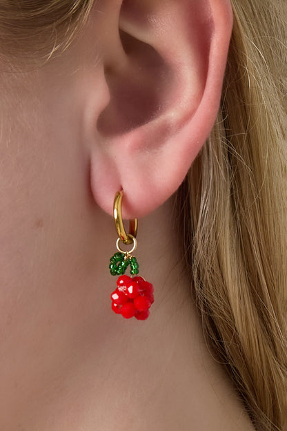 Close-up of a woman's ear wearing a gold hoop earring with red beaded cherry cluster and green bead leaf charm