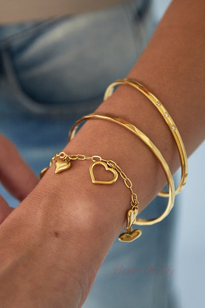 Closeup of wrist adorned with gold bangles, featuring mini diamond bangle and heart charm bracelet