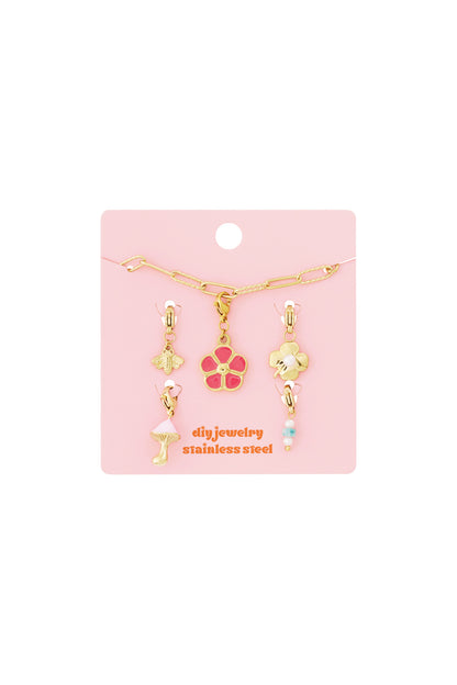 Gold link charm bracelet kit on pink card with bee, pink flower, clover, mushroom, and beaded charms.