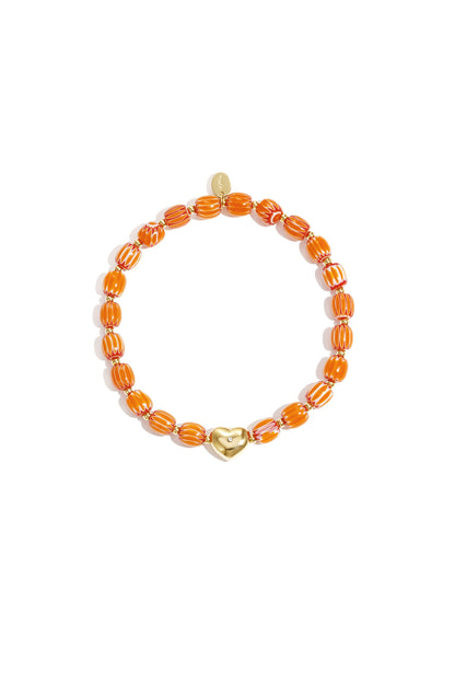 Orange and white striped beaded bracelet with gold heart charm laid flat on white background