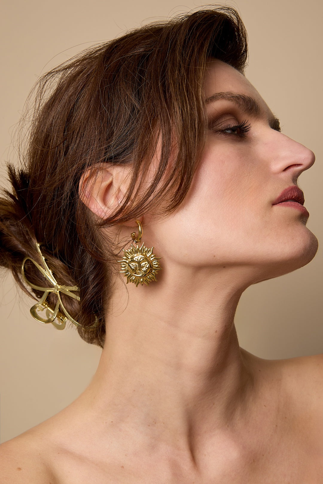 Woman wearing gold sun face drop earring showcasing side profile with hair clip