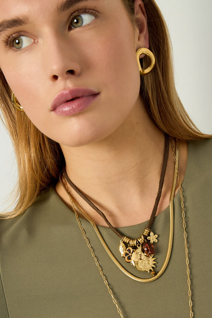 Side profile of model wearing the rope pendant necklace with matching gold earrings and layered chains