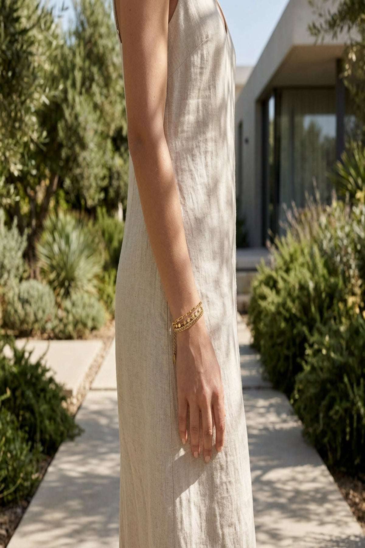 Slim female model wearing a tiny stainless steel bracelet on her wrist outdoors among greenery, showcasing its delicate and minimalist design.