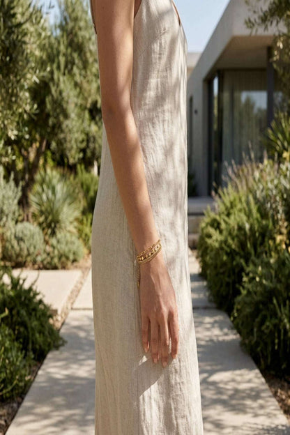 Slim female model wearing a tiny stainless steel bracelet on her wrist outdoors among greenery, showcasing its delicate and minimalist design.