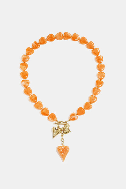 Orange heart-shaped bead necklace with gold-tone charms on white background