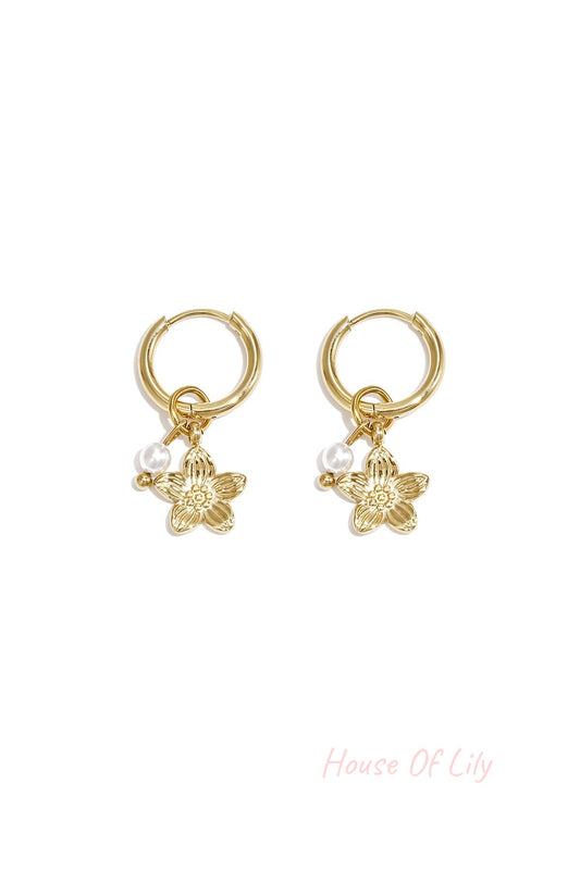Pair of gold hoop earrings with dangling gold flower charm and small white pearl bead on white background