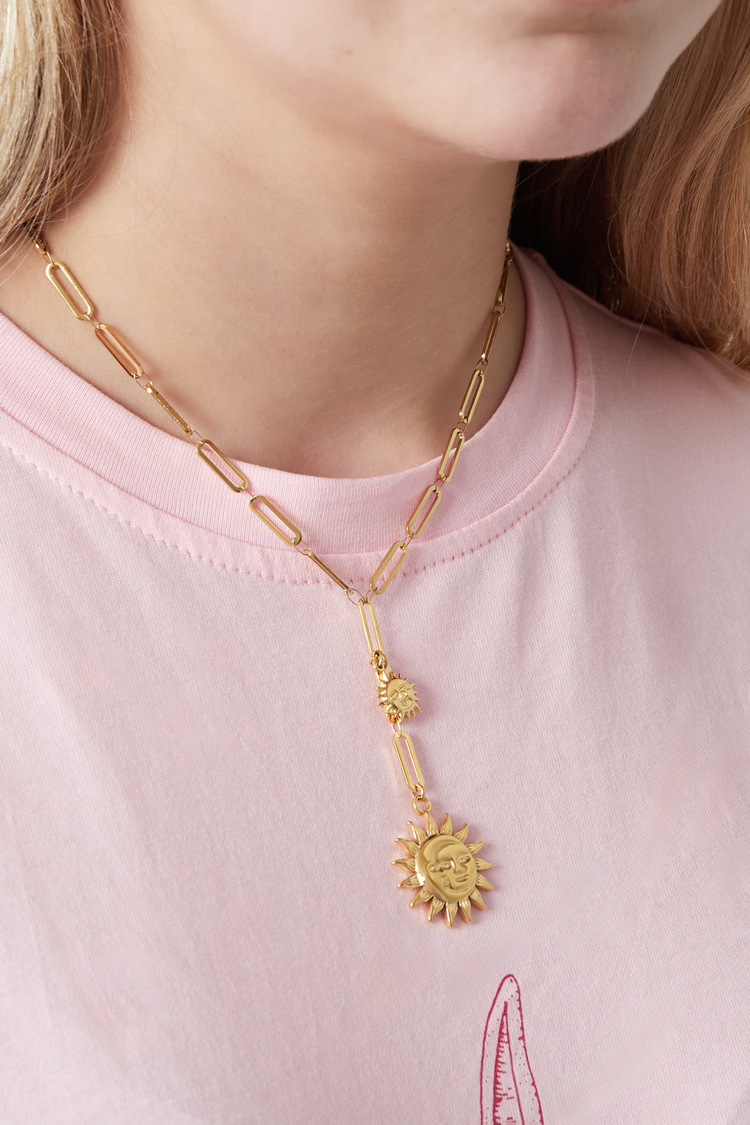 Close-up of gold dual sun pendant necklace worn with pink t-shirt showing chain and sun charms