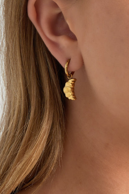 Close-up of a woman wearing gold-colored croissant charm hoop earring with natural hair