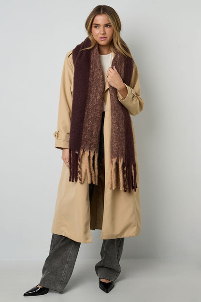 Model wearing brown gradient fringe scarf over beige trench coat, front view