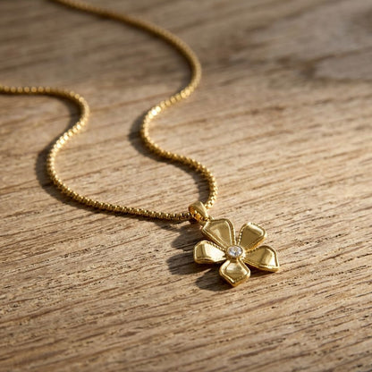 Dainty Floral Bloom Bestie necklace with zircon petals on a wooden surface, natural sunlight highlights its sparkle and floral design.