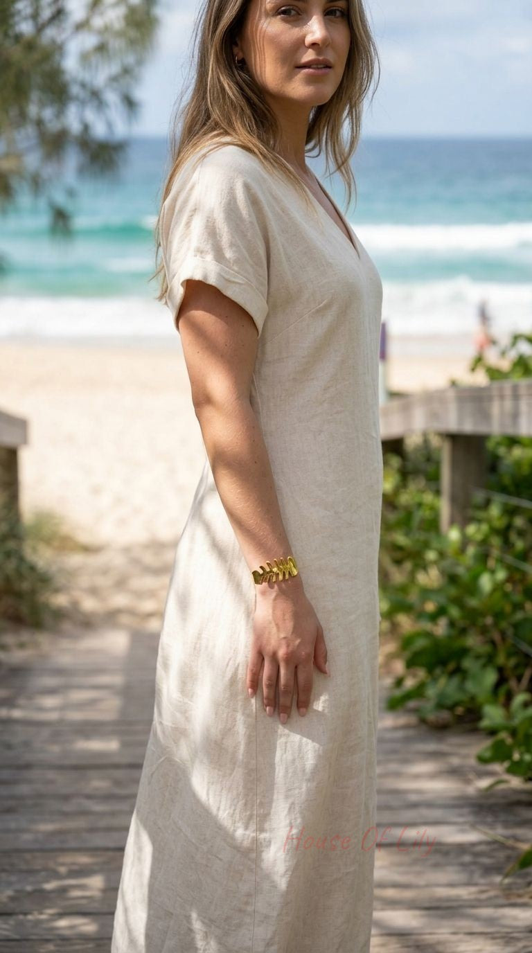Model on outdoor beach setting wearing a delicate gold fishbone cuff bangle on her wrist in natural daylight.
