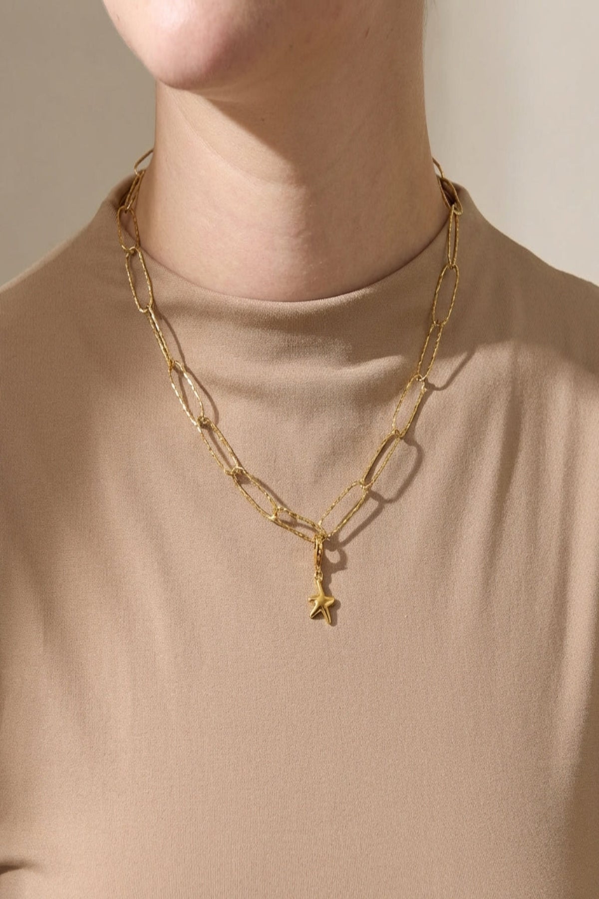 High-resolution image of model wearing a small, textured paperclip chain necklace with hammered finish, natural light highlighting its delicate design.