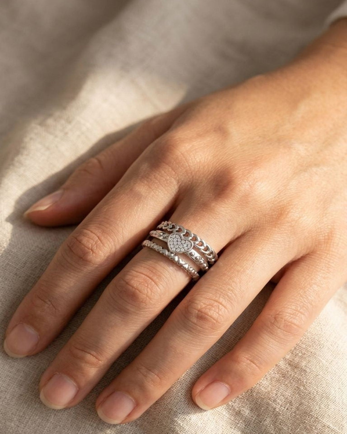 Small Dainty Heart Chain ring on a model's hand resting on soft fabric, showcasing the delicate multi-layered heart design and sparkle in warm sunlight.