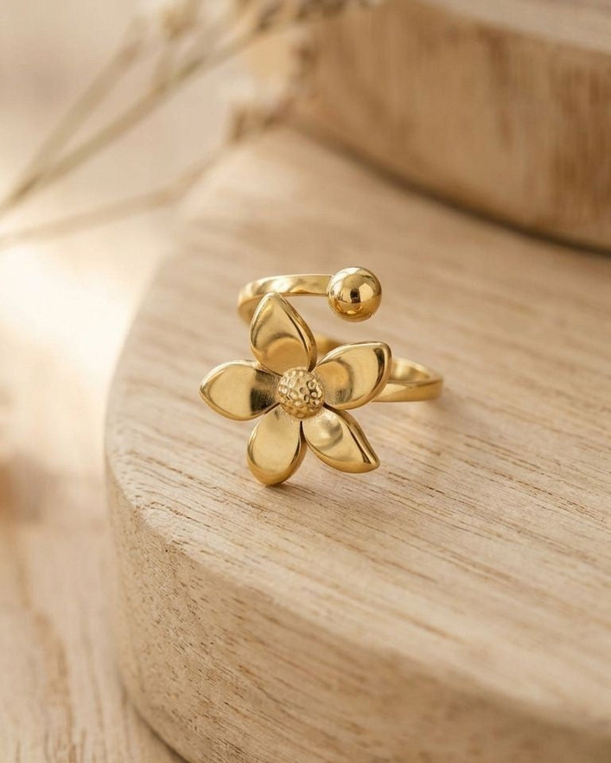 Close-up of the Gilded Bloom Statement ring with five-petal flower and polished sphere on a wooden surface