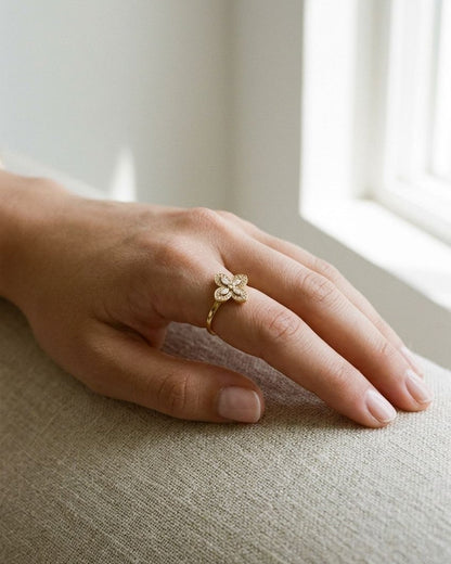Dainty gold clover statement ring with sparkling rhinestones worn on a finger resting on textured linen.