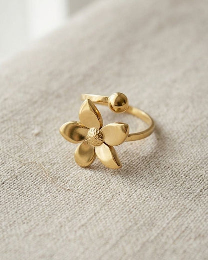 Delicate gold flower statement ring with five petals and polished sphere center on neutral textured surface