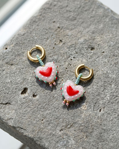Gold plated heart earrings with glazed beads resting on a grey stone surface.