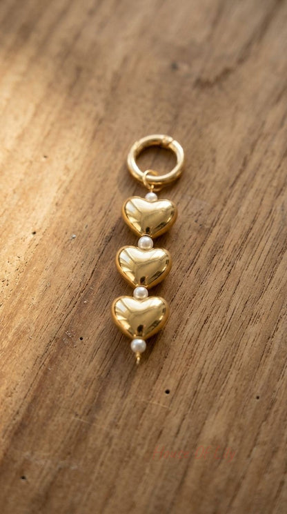 Close-up of Gold Heart Pearl Charm with three gold hearts and faux pearls displayed on textured wooden surface with warm natural light.