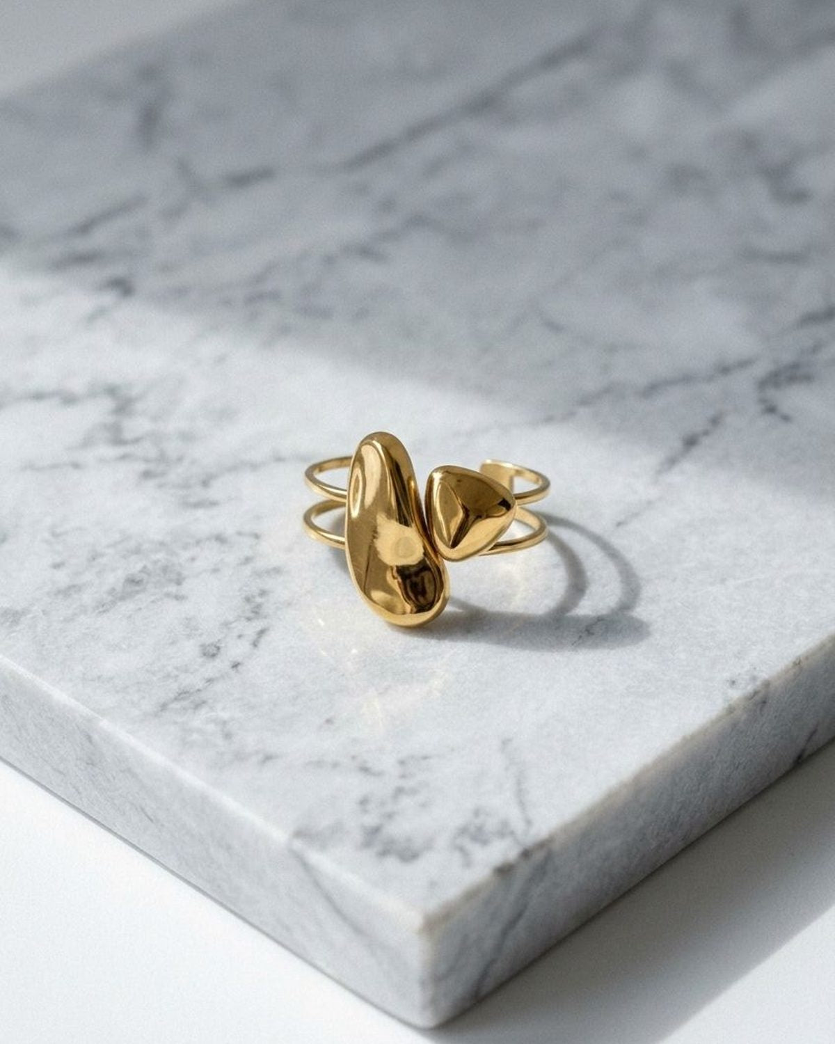 Gold organic statement cuff with irregular sculptural shapes resting on a light grey marble surface.
