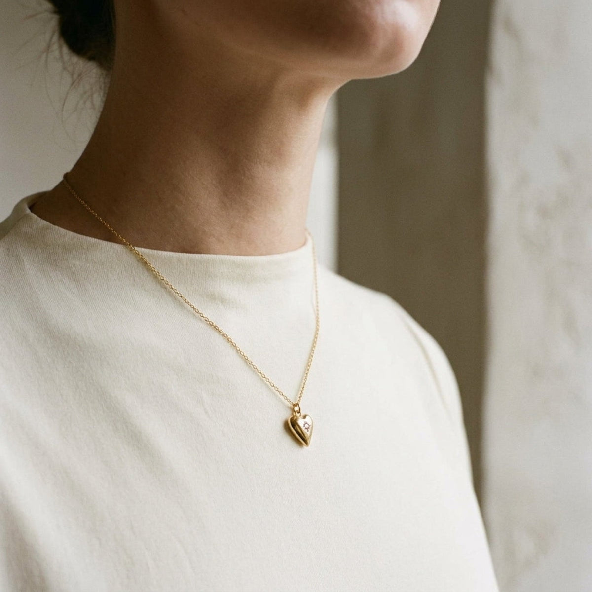 Close-up of a delicate gold-plated stainless steel heart pendant necklace with sparkling rhinestones, shown on a model's collarbone.