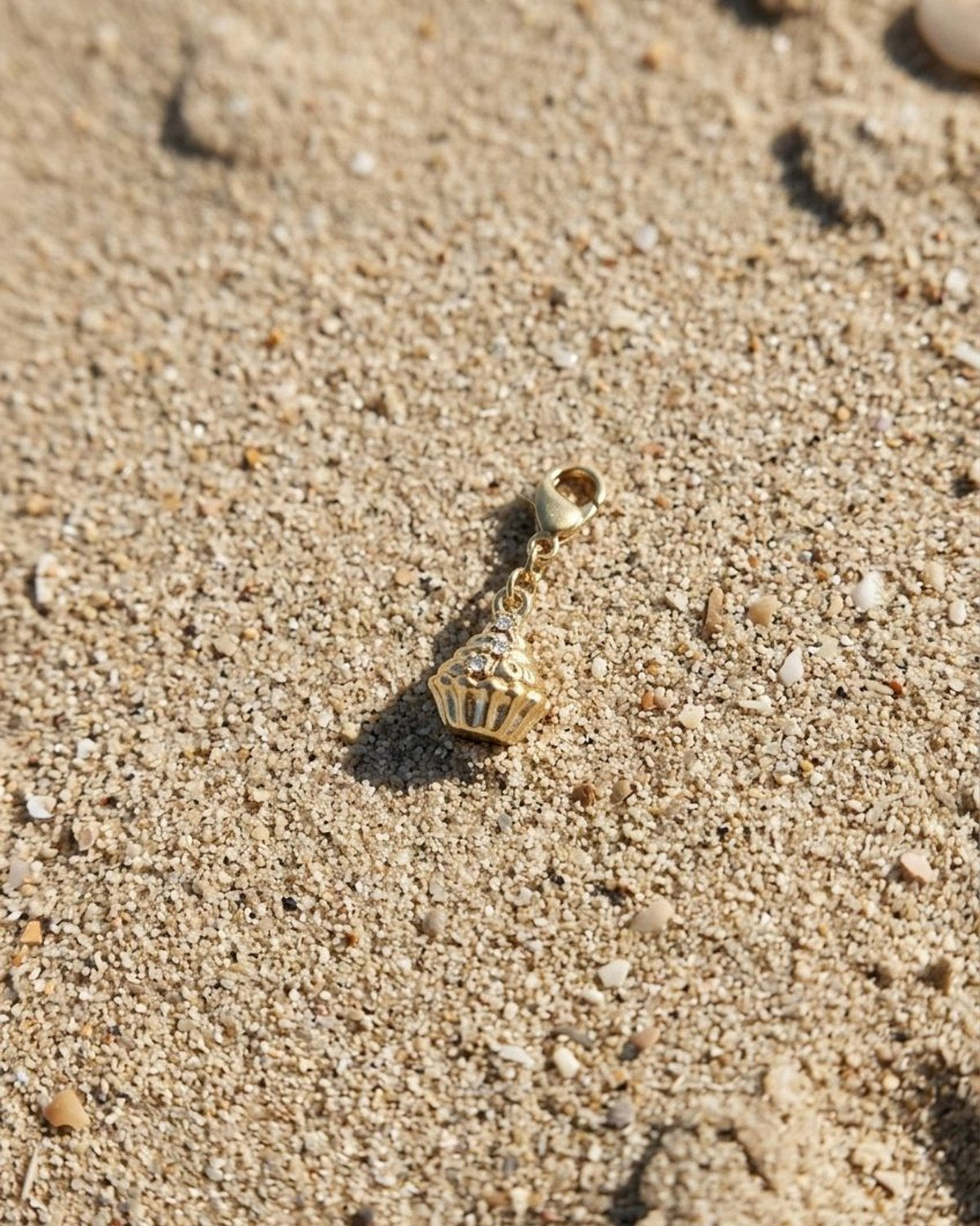 Gold rhinestone cupcake ring resting on a textured beige sandy beach surface.