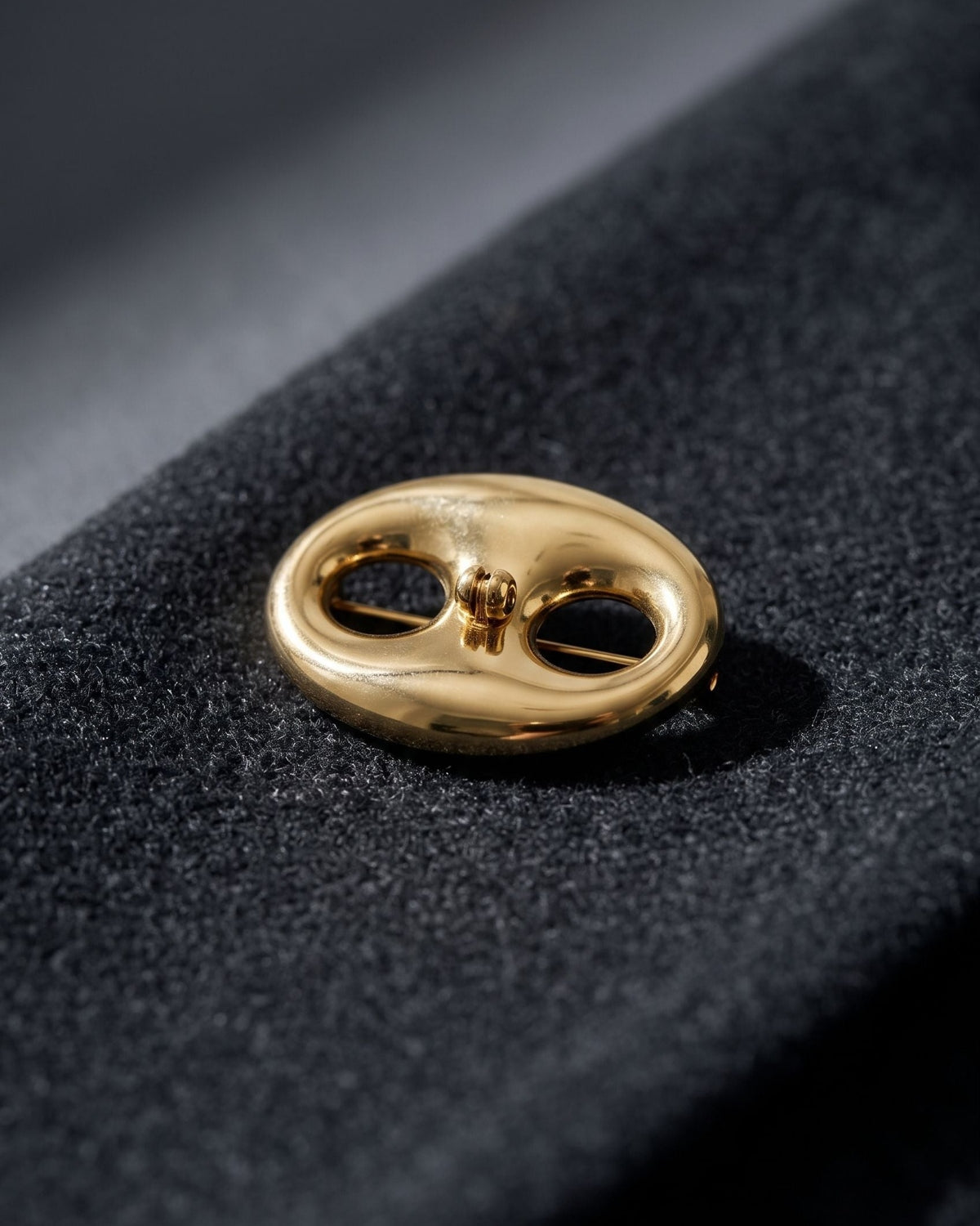 Gold irregular stainless steel brooch resting on textured dark charcoal wool fabric.