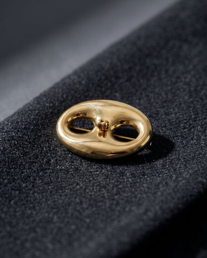 Gold irregular stainless steel brooch resting on textured dark charcoal wool fabric.